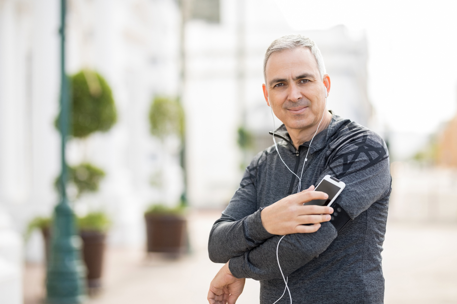 Confident mature man with earbuds and phone representing successful longevity program participant